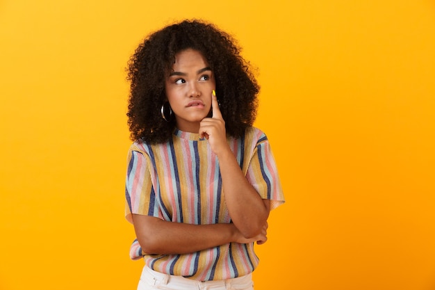 Chica linda africana joven pensativa posando aislada sobre espacio amarillo.