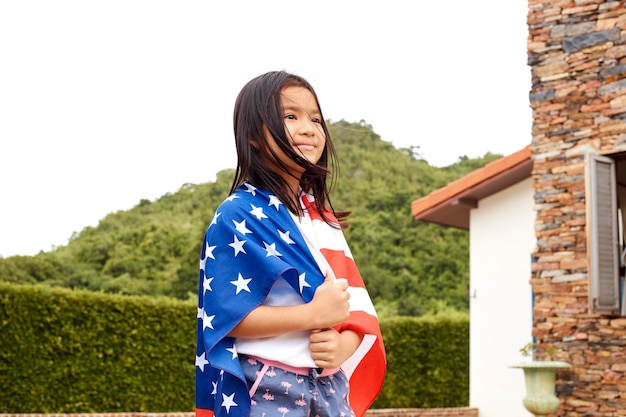 Foto chica linda con bandera estadounidense de pie contra la casa