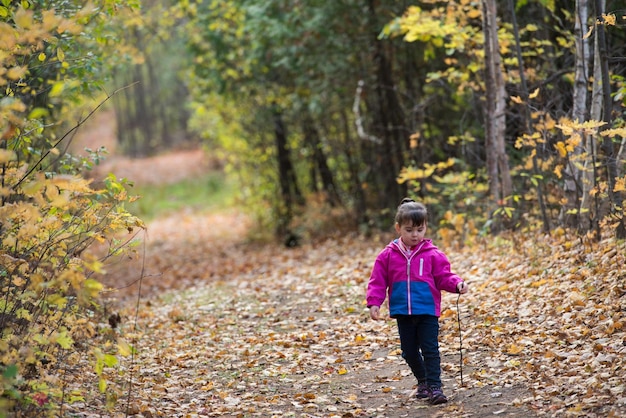 Chica linda caminando por un camino cubierto de hojas caídas durante el otoño