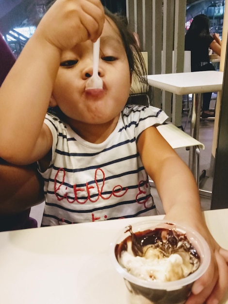 Foto una chica linda comiendo helado mientras está sentada en un restaurante