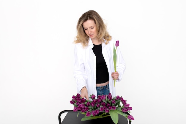 Una chica linda elige un tulipán morado para un ramo en la mesa Se encuentra en un fondo blanco