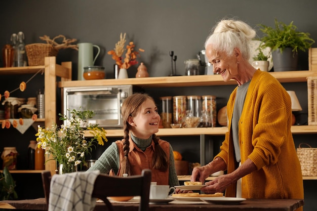 Una chica linda y feliz con colillas mirando a su abuela mientras toma té.