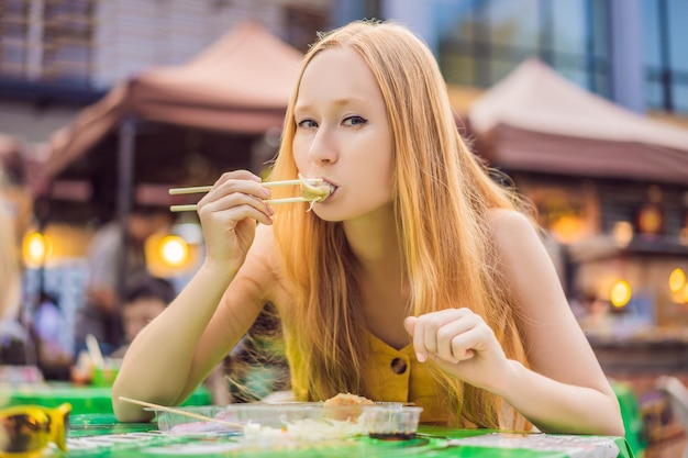 Chica linda feliz comiendo comida callejera y luciendo agradable en una pequeña feria tradicional