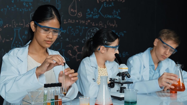 Una chica linda mirando bajo el microscopio mientras un estudiante hace un experimento de edificación