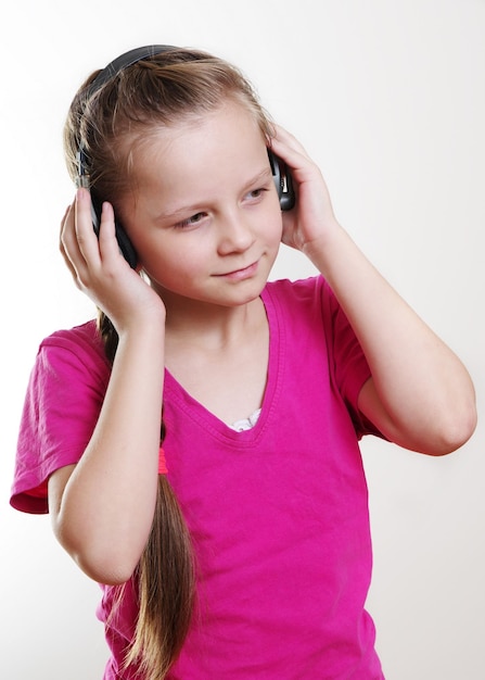 Foto chica linda mirando hacia otro lado mientras escucha música a través de auriculares contra un fondo blanco