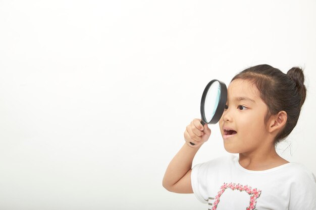 Foto una chica linda mirando a través de una lupa contra un fondo blanco