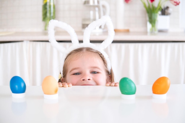 Chica linda con orejas de conejo en la cabeza jugando a la caza de huevos para la Pascua celebra la Pascua en casa