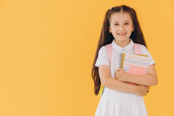 Foto chica linda de primer grado en uniforme blanco con mochila con cuadernos y libros