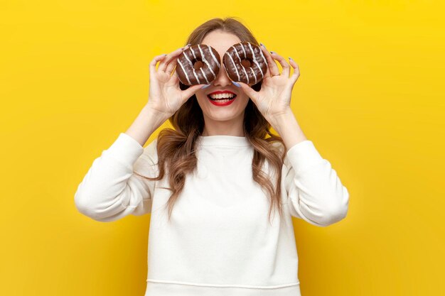 chica linda con rosquillas dulces muestra su lengua y hace caras en fondo aislado amarillo