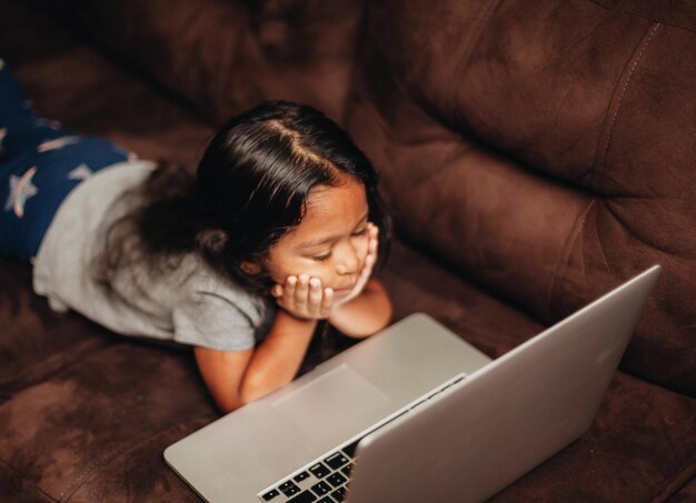 Una chica linda usando una computadora portátil mientras está acostada en el sofá en casa