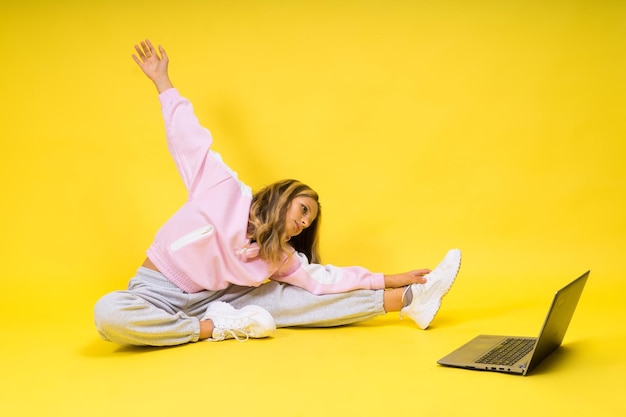 Chica en línea de fitness haciendo ejercicio de estiramiento en el piso sola con una computadora portátil en el estudio