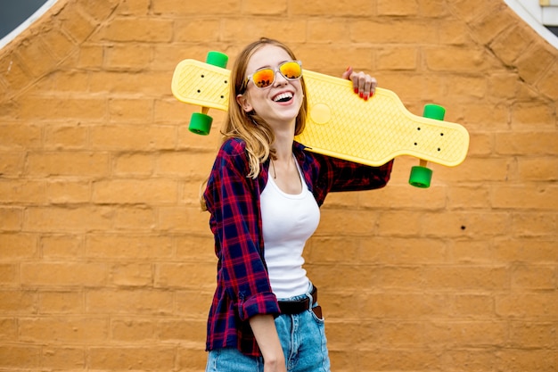 chica de longboard se encuentra junto a la pared de ladrillo