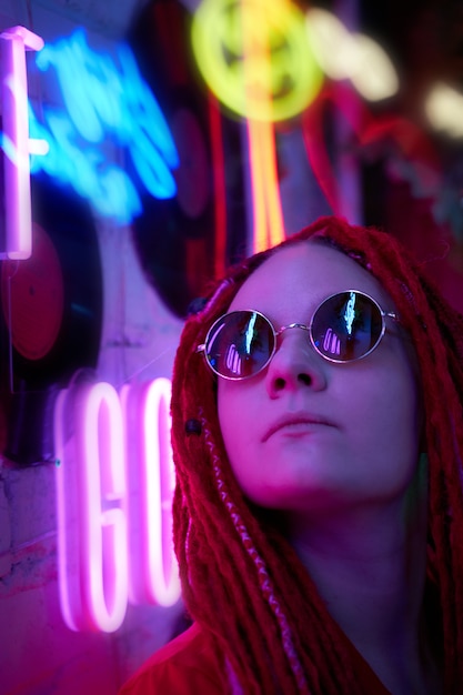 Chica con luces de neón, hermosa mujer con gafas de sol, con cabello rosado, con coletas de rastas,