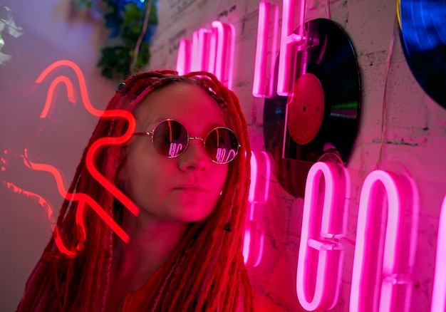 Chica con luces de neón, hermosa mujer con gafas de sol, con cabello rosado, con coletas de rastas,