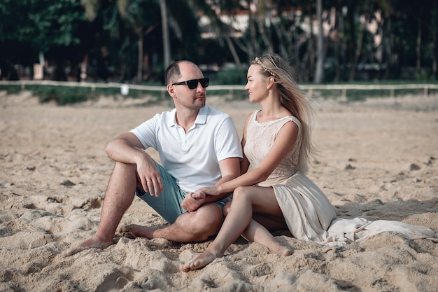 La chica luminosa y su novio se toman de la mano cariñosamente mientras están sentados en una playa de arena en Tailandia.
