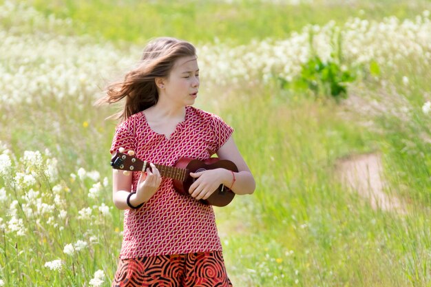 La chica de la madrugada camina por el prado con ukelele.