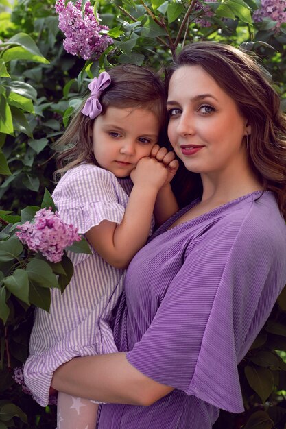 Foto chica con mamá en vestidos de color lila de pie junto a la lila