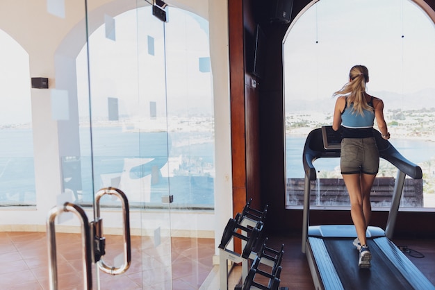 Chica en la mañana correr en la cinta en el gimnasio frente a una gran ventana en el fondo del mar