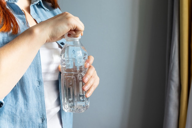 Chica manos abren una botella de agua en la habitación. Concepto de sed