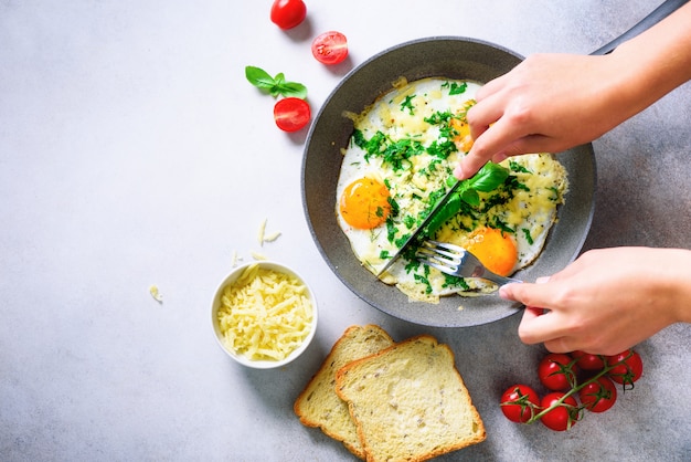 Chica manos arriba sartén con tres huevos cocidos, hierbas, queso, tomates