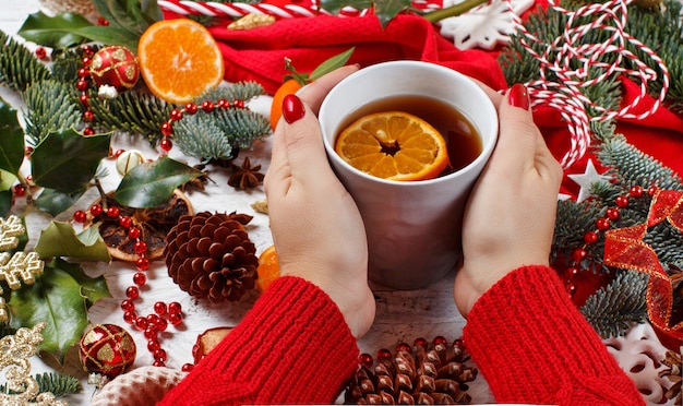 Chica manteniendo la taza de té con Navidad con adornos y ramas de abeto alrededor