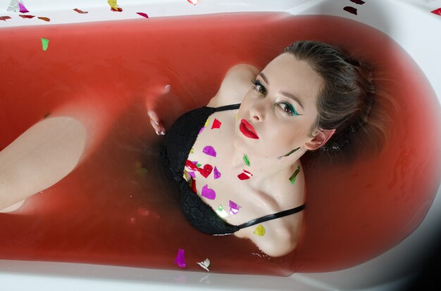 Chica con maquillaje brillante en un baño con agua roja.