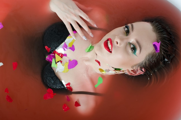 Foto chica con maquillaje brillante en un baño con agua roja.