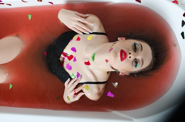 Chica con maquillaje brillante en un baño con agua roja.