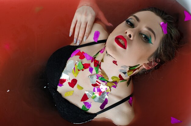 Foto chica con maquillaje brillante en un baño con agua roja.