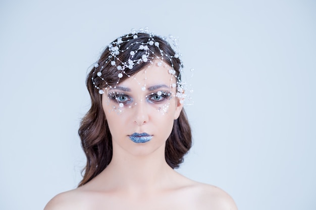 Chica con maquillaje creativo para el nuevo año. Retrato de invierno Colores brillantes, labios azules, cabello elegante con cristales, cuentas y gemas. ual art. Reina de nieve.