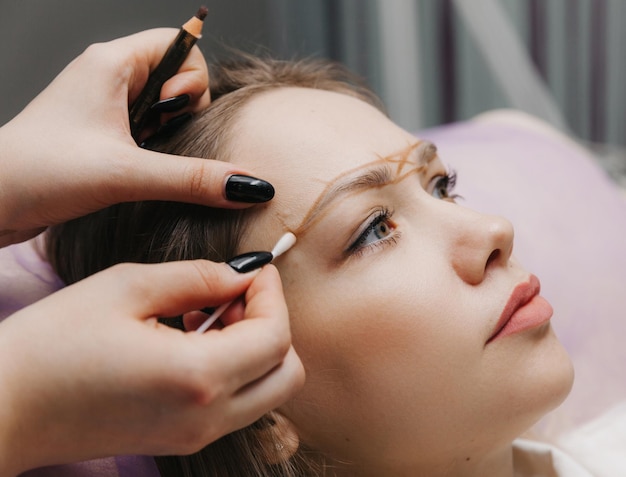 Chica con maquillaje permanente en las cejas La maquilladora hace marcas con un lápiz marrón para tatuarse las cejas