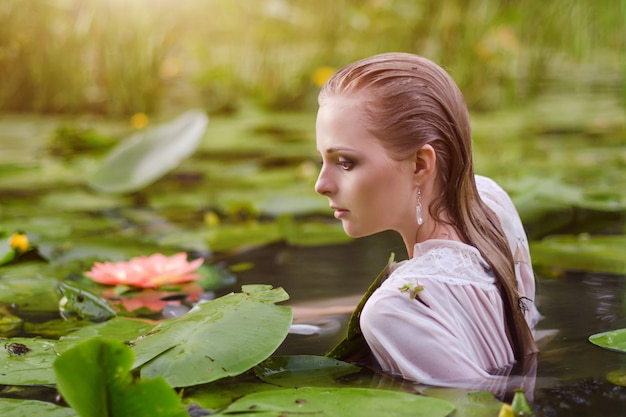 Chica con maquillaje suave en el lago entre lotos y nenúfares