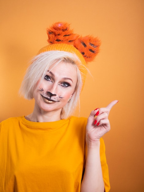 Una chica con maquillaje de tigre sobre un fondo naranja. Sonrisa divertida. Celebración del año nuevo del tigre