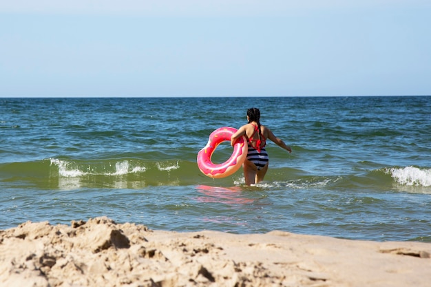 Chica en el mar con un salvavidas rosa en un día de verano