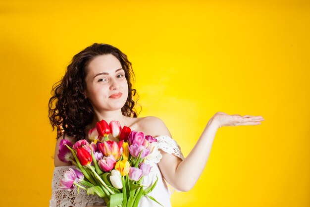 La chica maravillosa con ramo de tulipanes demuestra algo sobre fondo amarillo