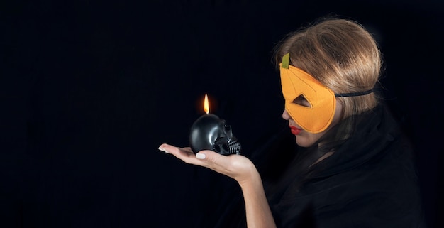 Chica con una máscara de calabaza sostiene una vela de calavera. Concepto de vacaciones de Halloween. Espacio de copia de banner.