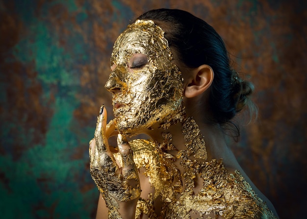 Chica con una máscara en la cara hecha de pan de oro Retrato de estudio sombrío de una morena sobre un fondo abstracto