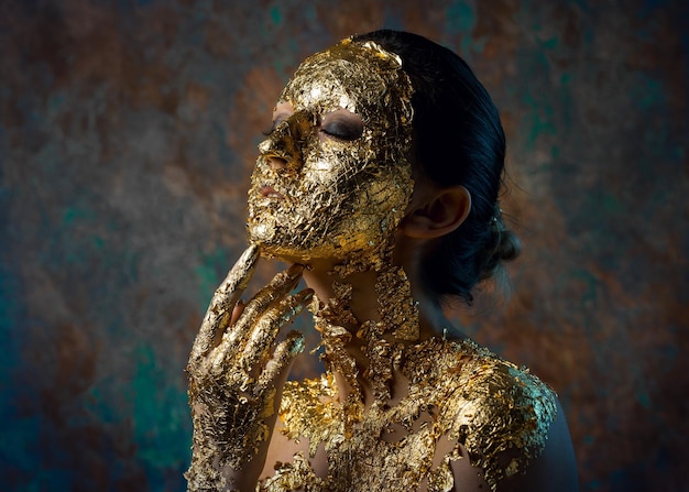 Chica con una máscara en la cara hecha de pan de oro Retrato de estudio sombrío de una morena sobre un fondo abstracto