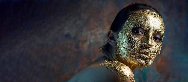 Chica con una máscara en la cara hecha de pan de oro Retrato de estudio sombrío de una morena sobre un fondo abstracto