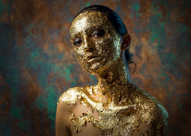 Chica con una máscara en la cara hecha de pan de oro Retrato de estudio sombrío de una morena sobre un fondo abstracto