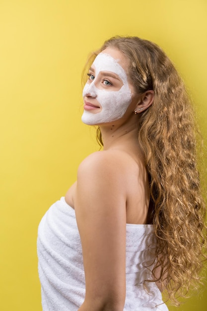 Chica con una máscara cosmética en la cara con una toalla blanca