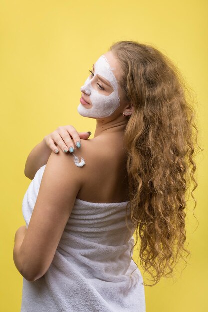 Chica con una máscara cosmética en la cara con una toalla blanca