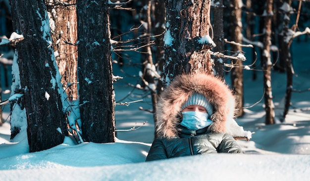 Chica en máscara debajo de un árbol con los ojos cerrados en el bosque de invierno.