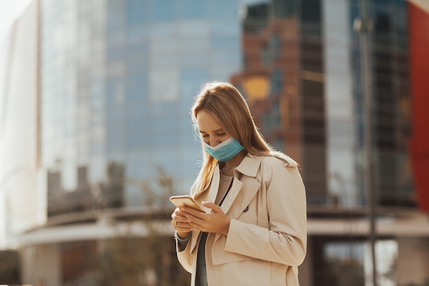 Chica en máscara está usando teléfono móvil.