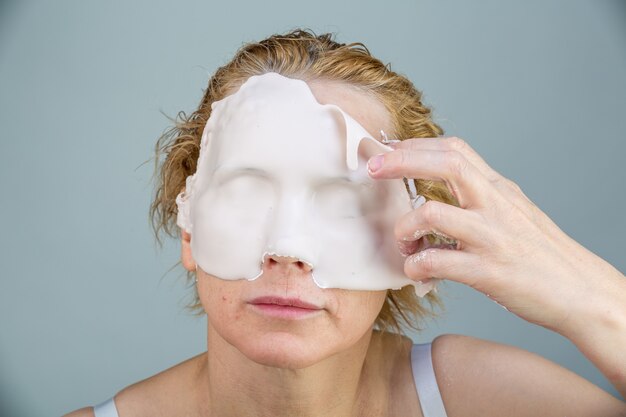 Chica con máscara facial mirando a cámara sobre fondo blanco. Procedimiento cosmético. Spa de belleza y cosmetología.