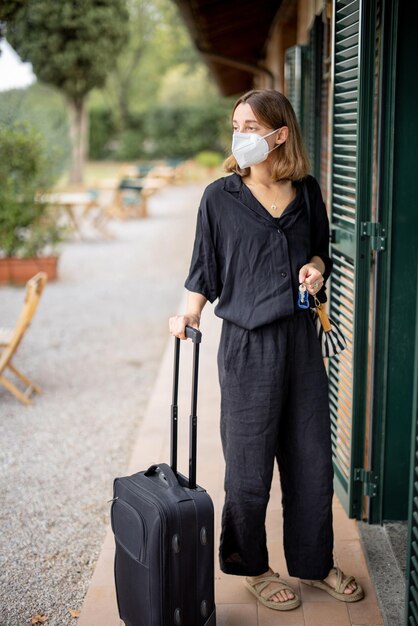 Chica en máscara médica con equipaje en la habitación del hotel