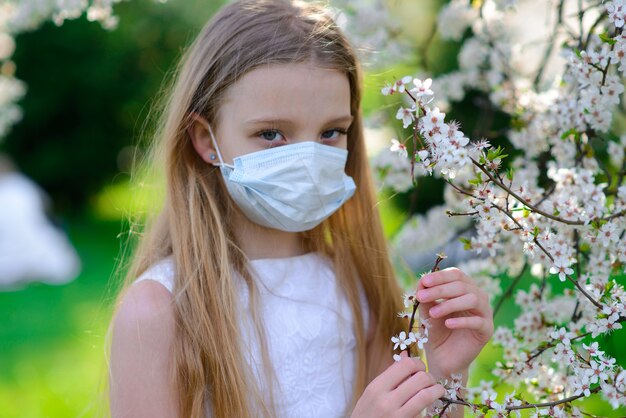 Chica en máscara médica en jardín de flores de primavera