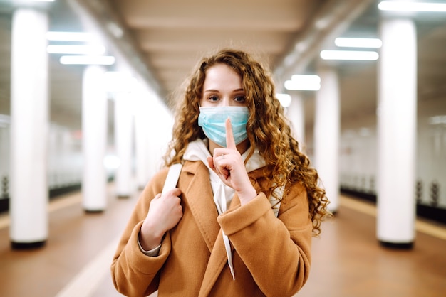 Foto chica con máscara médica protectora estéril en su rostro muestra un gesto: shh. silencio.