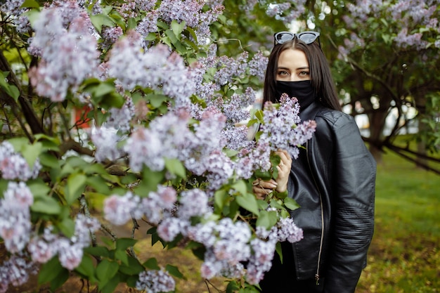 Chica en una máscara médica sobre un fondo de flores lilas. Máscara negra. Protección contra virus, gripe. Protección contra el coronavirus. epidemia de coronavirus