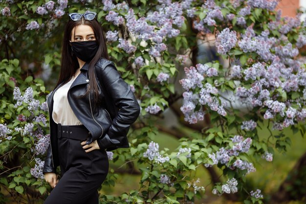 Chica en una máscara médica sobre un fondo de flores lilas protección de máscara negra contra el virus de la gripe